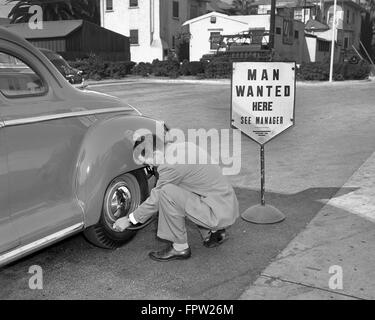 Anni Cinquanta uomo indossare tuta messa aria nel pneumatico automobile accanto all aiuto voluto firmare Foto Stock