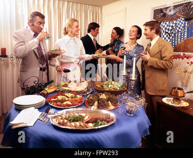 Anni Settanta tre coppie di uomini e donne a buffet cena mangiare bere parlando di ridere avente un buon tempo Foto Stock