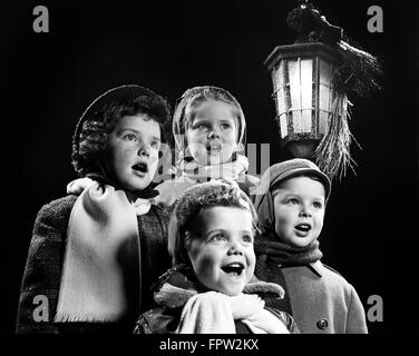 Anni Cinquanta quattro figli piccoli canti natalizi OUTDOOR dalla luce della lanterna Foto Stock