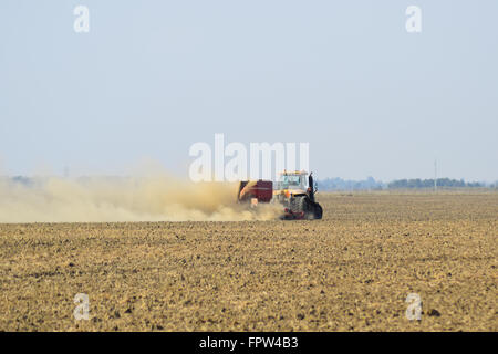 Il trattore corre sul campo e rende il fertilizzante nel terreno. Nuvole di polvere dal suolo asciutto del rimorchio del trattore. Fertilizzanti Foto Stock