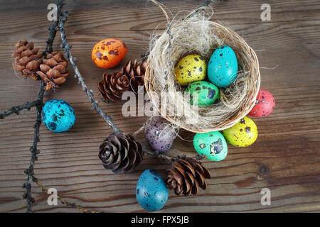 Luminose le uova di Pasqua su sfondo di legno. Pasqua colorata vita ancora con le uova nel nido e pigne. Sfondo di pasqua. Foto Stock