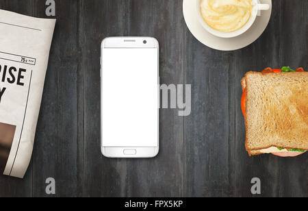 Smart Phone con display isolato per mockup sul tavolo. Quotidiani, caffè e sandwich sul tavolo. Vista dall'alto. Foto Stock
