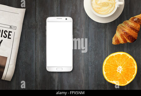 Smart Phone con display isolato per mockup sul tavolo. Quotidiani, caffè, croissant e arancione sul tavolo. Vista dall'alto. Foto Stock