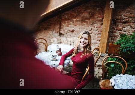 Giovane bella coppia elegante in un abito rosso nella storia di amore al vintage cafe con grandi finestre a tetto, ragazzo dà un fiore Foto Stock