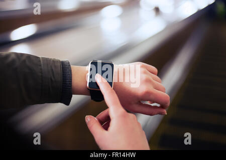 Femmina con la sua smart alla moda orologi da polso mentre cavalcate escalator in metropolitana. Questa persona è sempre collegato al social media e internet. Foto Stock