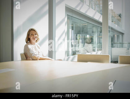 Ritratto sorridente imprenditrice nella soleggiata sala conferenze Foto Stock