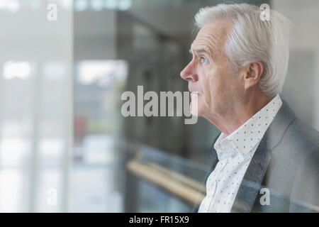 Imprenditore pensieroso a guardare fuori dalla finestra di ufficio Foto Stock