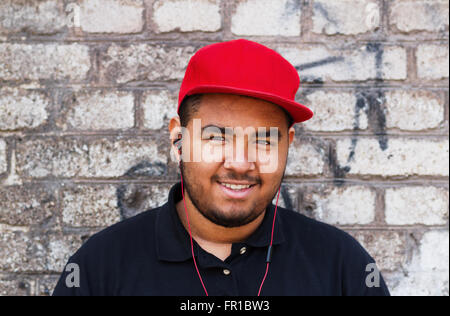 Ritratto di un giovane ragazzo africano godendo la musica attraverso il suo red headphones. Foto all'aperto su un muro di mattoni in background Foto Stock