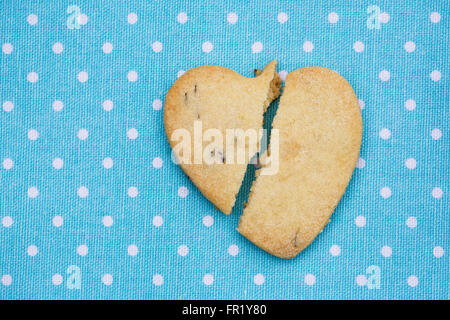 Un cuore spezzato biscotto a forma su un blu a macchie sullo sfondo. Foto Stock