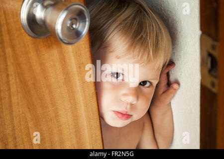 Piccola bionda bambina apre la porta e guarda al di fuori Foto Stock