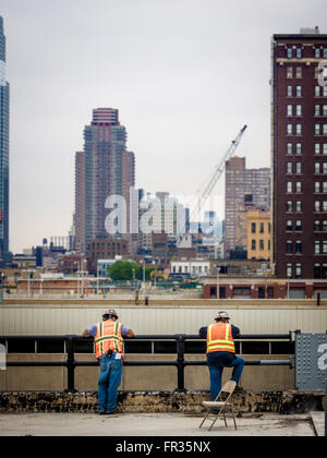 Due lavoratori sul sito in costruzione avente una pausa e guardando oltre le ringhiere, New York City, Stati Uniti d'America. Foto Stock