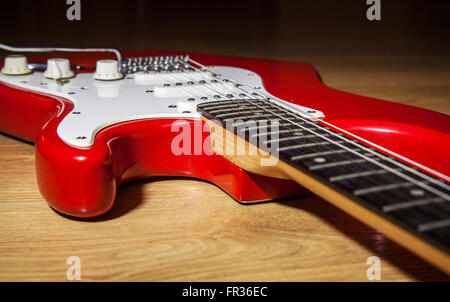 Parte del corpo di rosso stringa 6 chitarra elettrica sdraiato sul pavimento in legno closeup Foto Stock