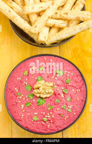 Hummus di barbabietole in una ciotola nero e bastoni di pane su una piastra di ardesia Foto Stock