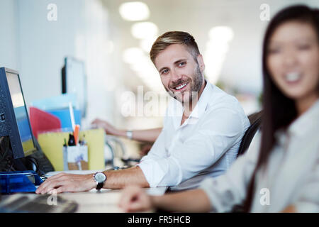 Imprenditore sorridente al computer in ufficio Foto Stock