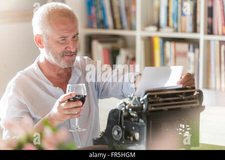 Senior uomo beve il vino a nastri inchiostratori per macchine da scrivere in studio Foto Stock