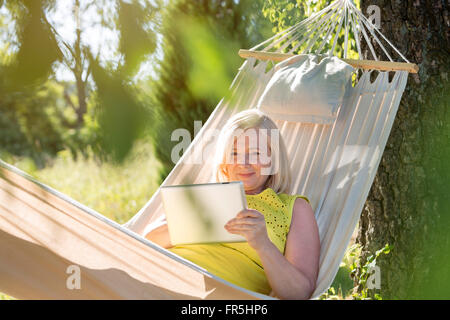 Donna senior con tavoletta digitale e per rilassarsi in estate amaca Foto Stock