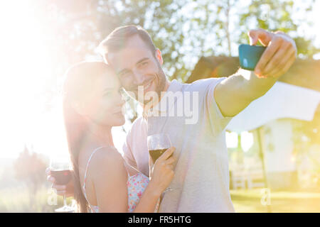 Coppia giovane con vino prendendo selfie nel cortile soleggiato Foto Stock