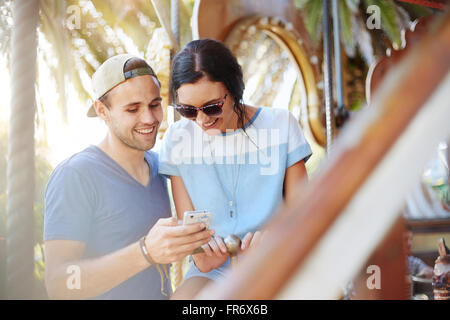 Coppia giovane texting con un telefono cellulare al parco di divertimenti Foto Stock