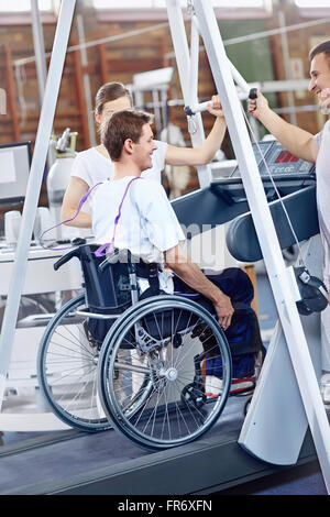 Fisioterapisti guidare l uomo in sedia a rotelle su tapis roulant Foto Stock