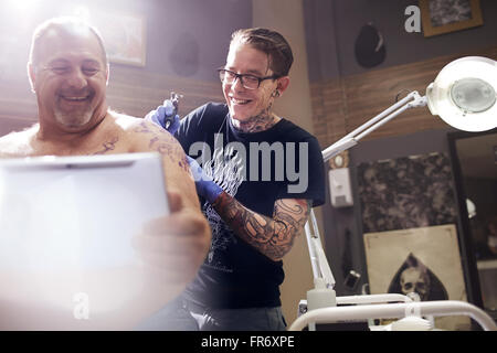 Uomo sorridente con tavoletta digitale getting spalla tattoo Foto Stock