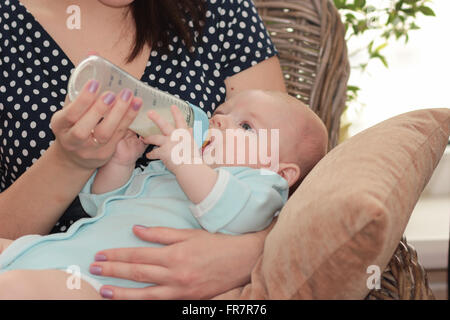 Madre a casa alimentazione bambino con una bottiglia di latte Foto Stock