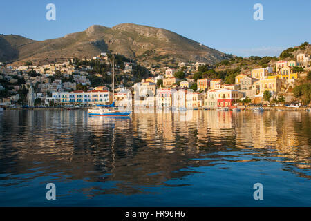 Gialos, Symi, Egeo Meridionale, Grecia. Vista su tutta la baia Harani presso sunrise, case colorate riflessa nell'acqua. Foto Stock