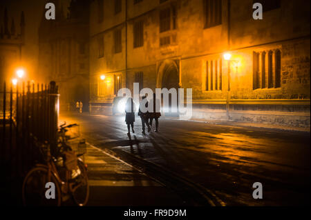 Tre stagliano gli studenti a piedi passato biblioteca Bodleian Library nella notte tempo verso Radcliffe Camera in Oxford, Regno Unito Foto Stock