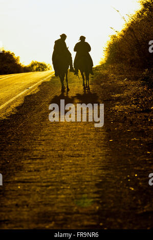 Tramonto e cowboy a cavallo sulla strada attraverso la savana Foto Stock