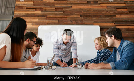 Gruppo di colleghi avente una sessione di brainstorming in sala conferenze. Giovane uomo che spiega i piani aziendali per i colleghi durante il m Foto Stock