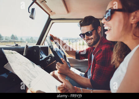Felice coppia giovane con una mappa in auto. Uomo sorridente e donna usando la mappa su roadtrip. Foto Stock