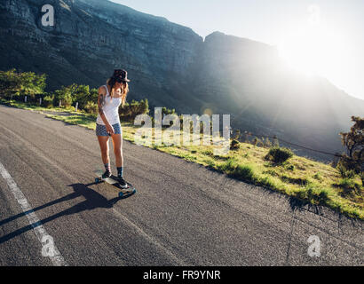 Giovane donna pattinaggio all'aperto sulla strada rurale. Surf femmina su un giorno d'estate. Foto Stock