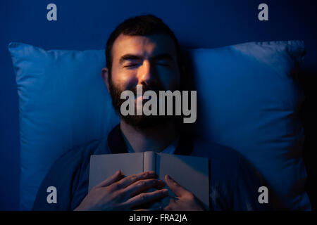 Uomo sorridente dorme con un libro sul suo petto Foto Stock