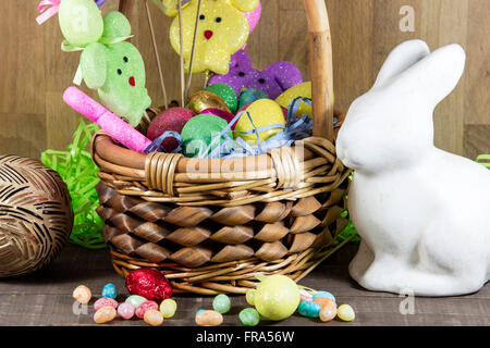 Pasqua cesto pieno di uova colorate e coniglietti, con la caramella sul piano del tavolo Foto Stock