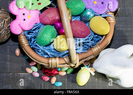 Pasqua cesto pieno di uova colorate e coniglietti, con la caramella sul piano del tavolo Foto Stock