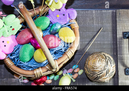 Pasqua cesto pieno di uova colorate e coniglietti, con la caramella sul piano del tavolo Foto Stock