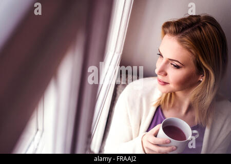 Donna sul davanzale tenendo una tazza di tè Foto Stock