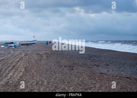 Persone lontane e barche sulla spiaggia tempestosa in inverno, Cley North Norfolk REGNO UNITO Foto Stock