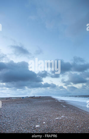 Persone lontane e barche sulla spiaggia tempestosa in inverno, Cley North Norfolk REGNO UNITO Foto Stock