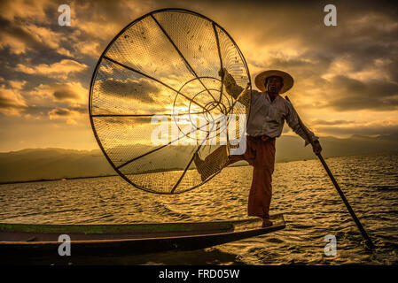 Pescatore birmano la pesca su una tradizionale barca di bambù con un netto fatti a mano di sunrise Foto Stock