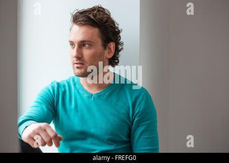 Bello pensieroso giovane uomo seduto e guardando la finestra su sfondo bianco Foto Stock