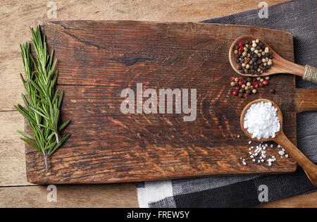 Sale e pepe in cucchiai di legno e rosmarinus sul tagliere di legno, vista dall'alto Foto Stock