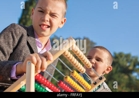 Si torna a scuola due confuso ragazzi piccoli giocando con legno abacus nel parco. Uno intorno sette altri quattro. Foto Stock