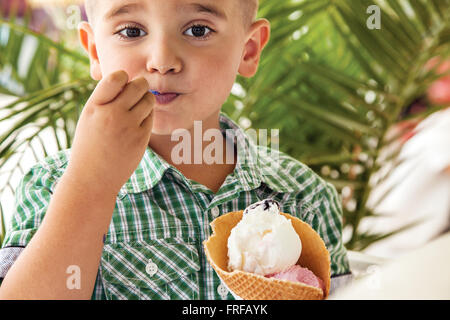 Giovane ragazzo a mangiare il gelato in un parco di fronte a un albero di palma. Foto Stock