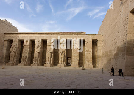 Le protezioni aspettano i turisti vicino Ramessid colonne del peristilio corte presso gli antichi egiziani sito di Medinet Habu (1194-1163BC), il tempio mortuario di Ramesse III a Luxor, la Valle del Nilo in Egitto. Medinet Habu è un nuovo importante periodo del regno di struttura nella West Bank di Luxor in Egitto. A parte la sua dimensione e la sua importanza architettonica ed artistica, il tempio è probabilmente meglio conosciuto come sorgente di inscritto rilievi raffiguranti l'avvento e la sconfitta dei popoli del mare durante il regno di Ramesse III Secondo il paese del Ministero del Turismo, i visitatori europei in Egitto è basso fino a un massimo di 80 Foto Stock