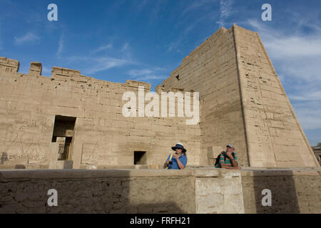 Turisti europei in prossimità del primo pilone presso gli antichi egiziani sito di Medinet Habu (1194-1163BC), il tempio mortuario di Ramesse III a Luxor, la Valle del Nilo in Egitto. Medinet Habu è un nuovo importante periodo del regno di struttura nella West Bank di Luxor in Egitto. A parte la sua dimensione e la sua importanza architettonica ed artistica, il tempio è probabilmente meglio conosciuto come sorgente di inscritto rilievi raffiguranti l'avvento e la sconfitta dei popoli del mare durante il regno di Ramesse III Foto Stock