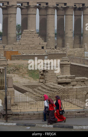 Giovani donne egiziane a piedi nella parte anteriore delle antiche colonne egiziane del Tempio di Luxor, Luxor, la Valle del Nilo in Egitto. Il tempio dietro fu costruito da Amenhotep III, completato da Tutankhamon poi aggiunti a da Ramses II. Verso la parte posteriore è un granito santuario dedicato ad Alessandro il Grande e in un'altra parte, era un accampamento romano. Il tempio è stato quasi in uso continuo come un luogo di culto fino ad oggi. Foto Stock