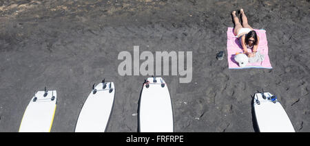 A Las Palmas di Gran Canaria Isole Canarie Spagna, 22 marzo 2016. Meteo: una giovane donna a prendere il sole e guardare il telefono cellulare vicino a tavole da surf sulla principale spiaggia della città di Las Palmas durante le vacanze di Pasqua in una gloriosa martedì mattina su Gran Canaria. Regno Unito premere viene segnalato che il Primo Ministro David Cameron e la famiglia sono in volo per le isole Canarie (Lanzarote) il 24 marzo per le loro vacanze di Pasqua Foto Stock