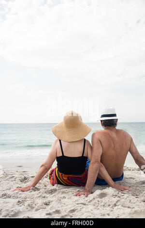 Vista posteriore della coppia senior seduto sulla spiaggia Foto Stock