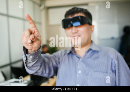 Uomo in un casco di realtà virtuale e ciò punti dito verso l'alto. Foto Stock