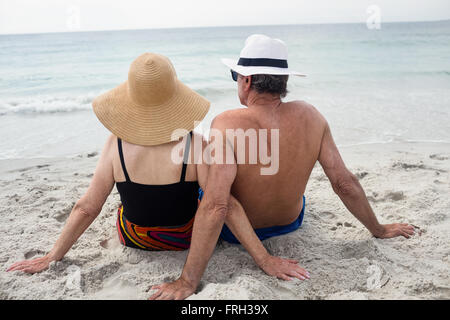 Vista posteriore della coppia senior seduto sulla spiaggia Foto Stock